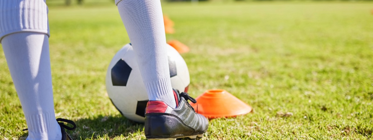 Legs of young person wearing cleats and about to kick a soccer ball